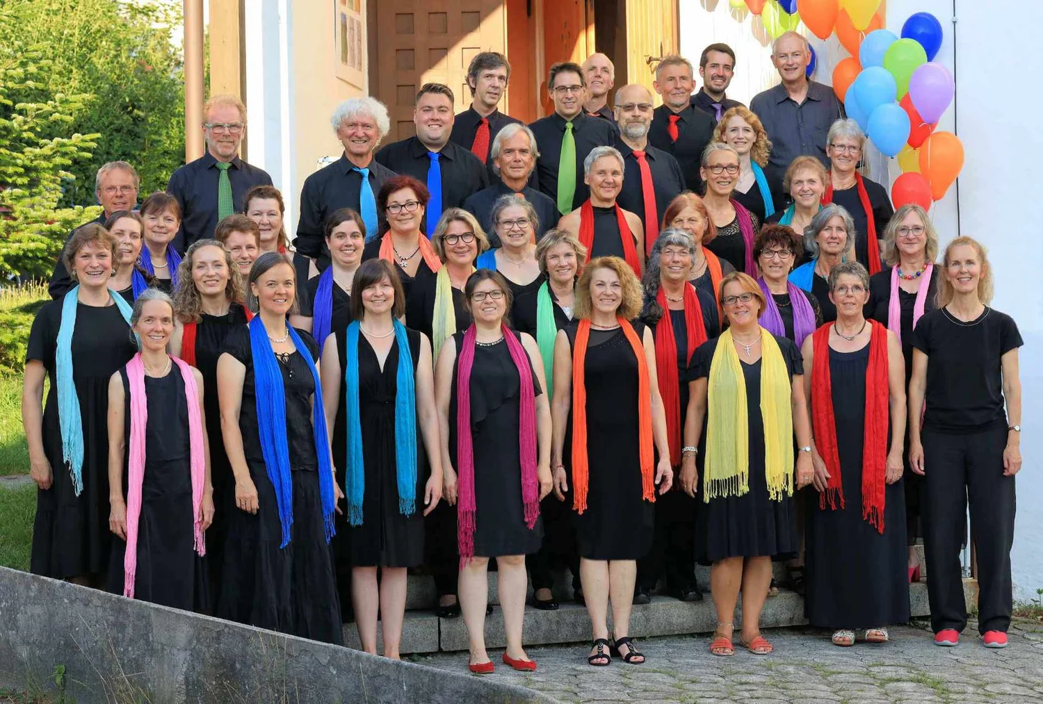 Der Chor mit bunten Schals und einem Regenbogen aus Luftballons.